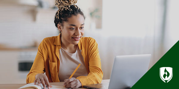 smiling woman looking at laptop and writing in a notebook