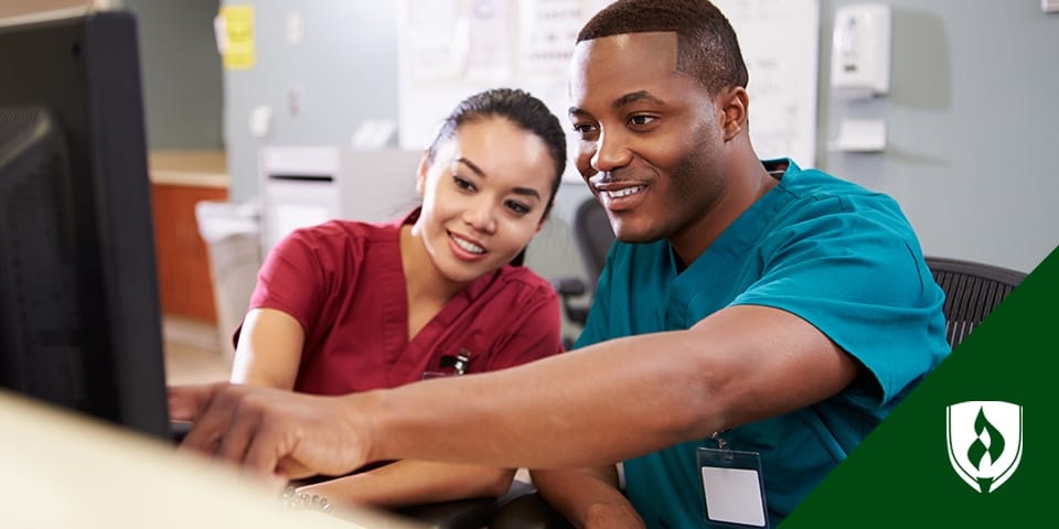 One nurse helping another with a computer at a nurse's station