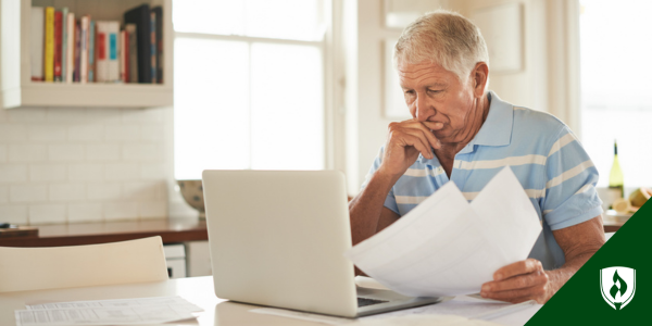 A small business owner stares into his computer with papers in hand