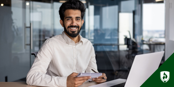 A medical coder holding a notebook smiles in front of his computer