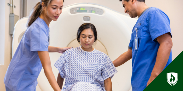 Two radiologic technologists help someone lie down for a scan