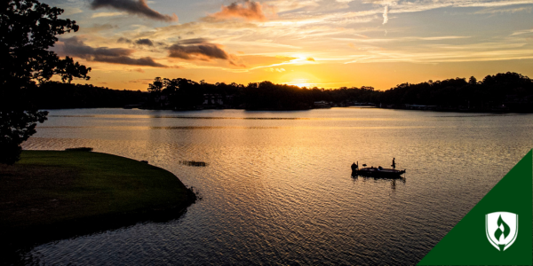 Someone stands up in a boat on a lake during sunrise