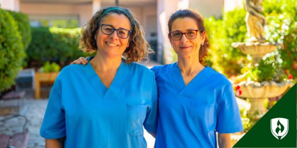 Two nurses pose outside their healthcare facility