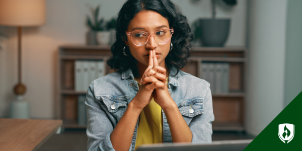 A student sits thinking in front of her computer at home