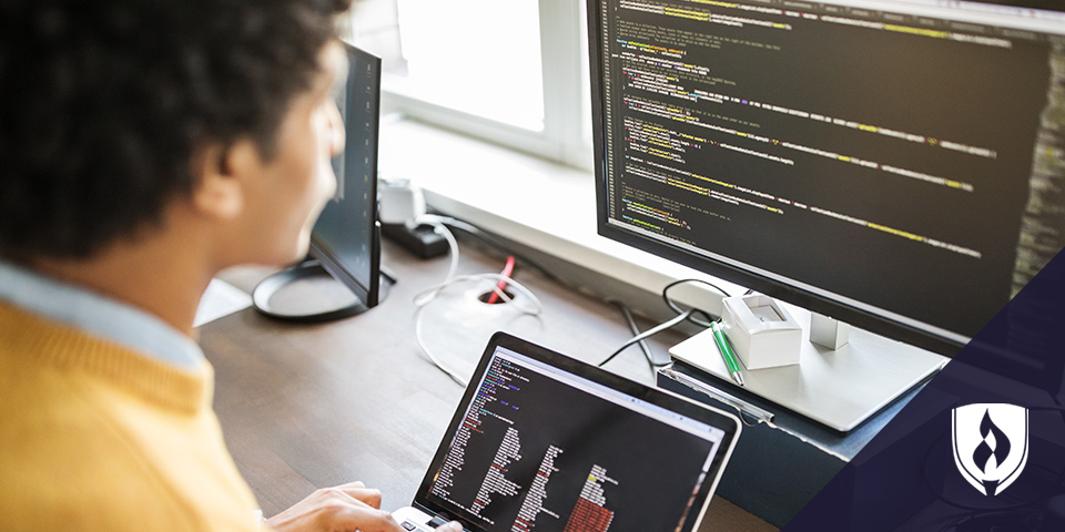 man writing code on laptop and monitor