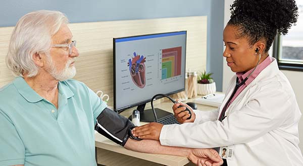 male nurse practitioner holding clipboard standing by man in hospital bed