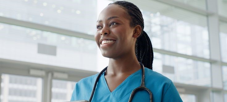 smiling nurse wearing scrubs with tablet in hand and stethoscope around neck